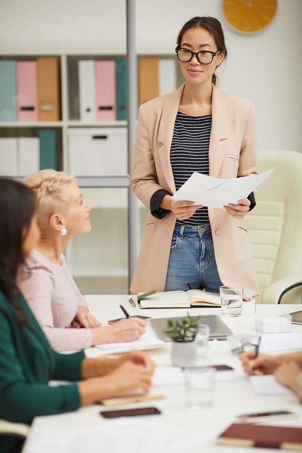 asian woman standing at table making presentation at business meeting