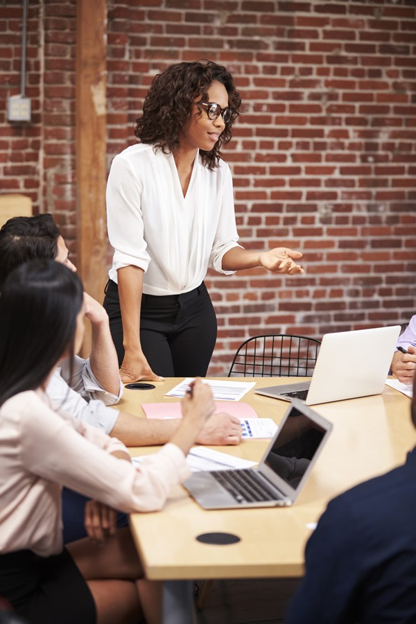business-woman-leads-meeting Businesswoman Standing And Leading Office Meeting Around Table