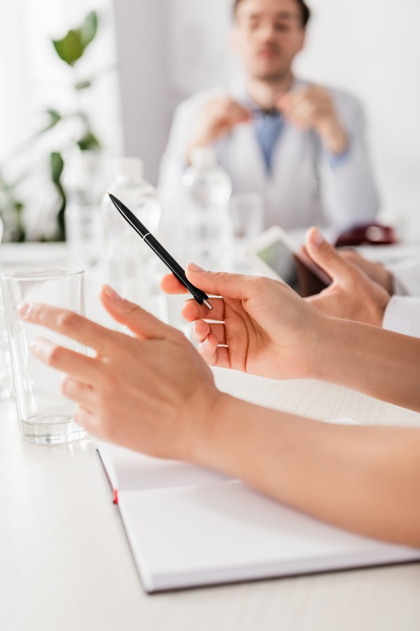 Doctor holding pen near notebook and colleagues on blurred foreground at table