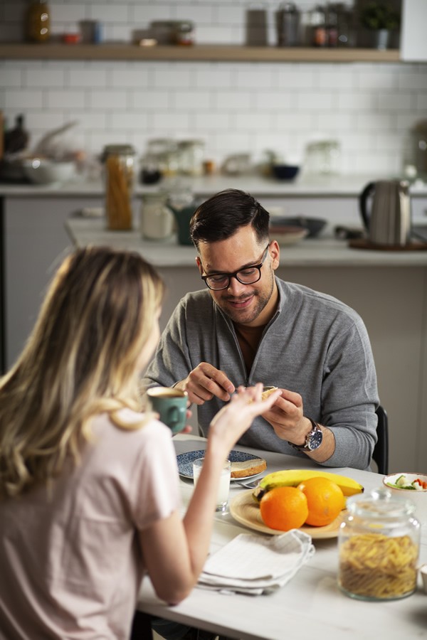 Happy man enjoying his breakfast with his girlfriend. Loving young couple drinking coffee and eating sandwich at home