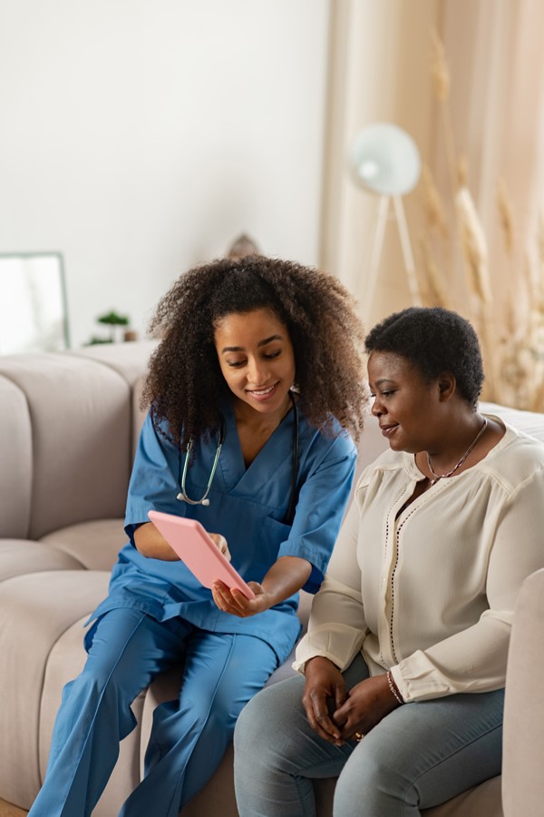 Curly-haired nurse showing online news to elderly lady